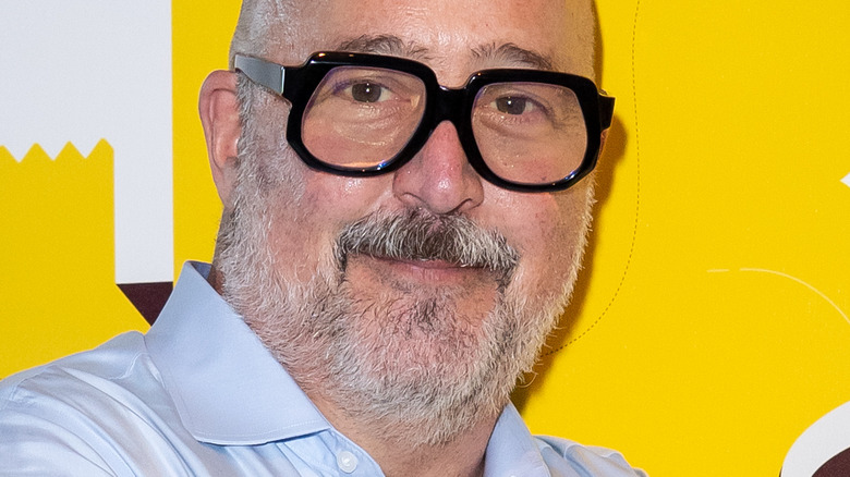 Andrew Zimmern with slight smile wearing thick-rimmed glasses