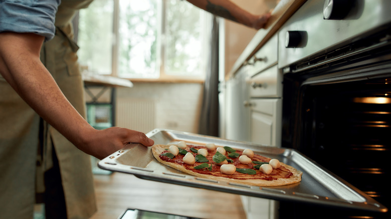 Pizza on a baking tray being put in the oven