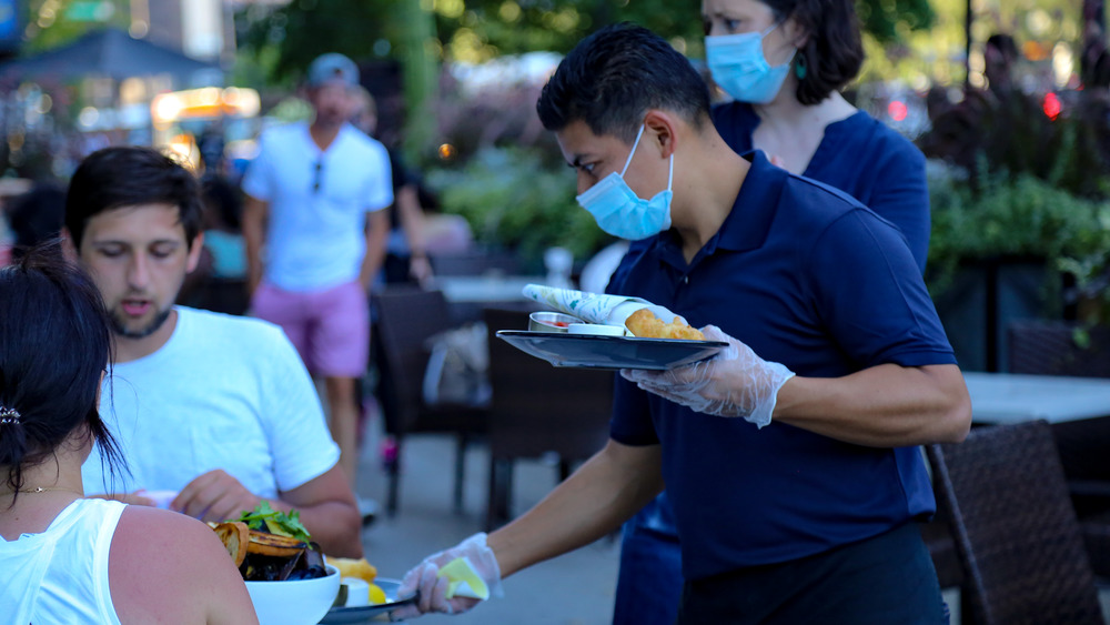 Waiter in face mask serves diners