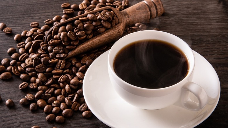 Coffee in white cup and saucer on table with beans