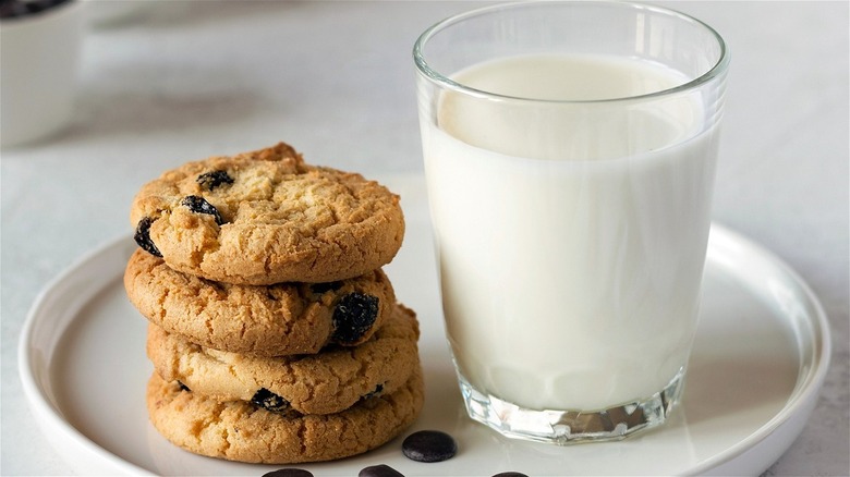 Cookies with raisins stacked next to glass of milk