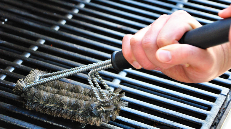 Hands holding grill brush cleaning grill