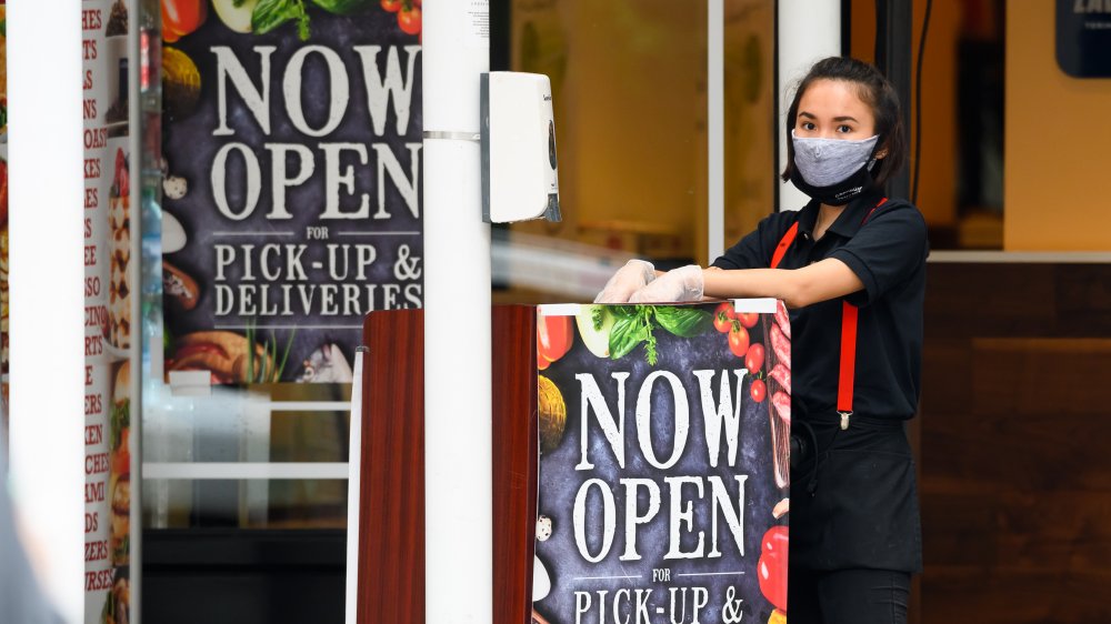 Female restaurant employee with face mask by open sign