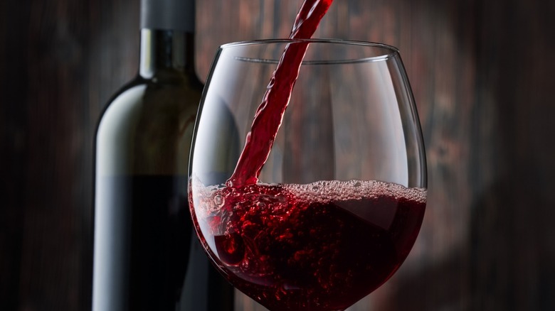 Red wine being poured into a glass with a bottle behind it