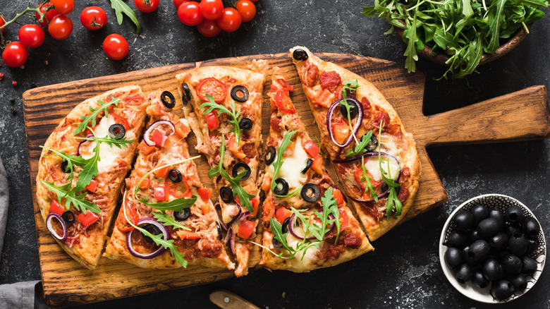 Top view of vegetable pizza on wooden board next to olives