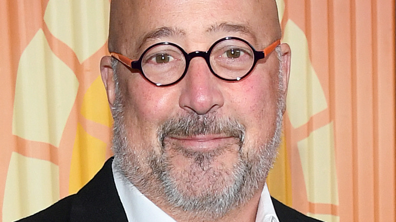 Andrew Zimmern wearing glasses against orange background