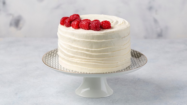  pastel blanco en un plato con glaseado de crema de mantequilla y cubierto con frambuesas