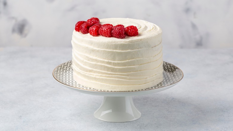 white cake on a platter with buttercream frosting and topped with raspberries