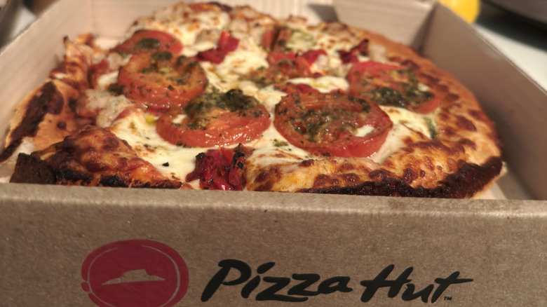 A pizza with tomato and cheese in a Pizza Hut-branded pizza box