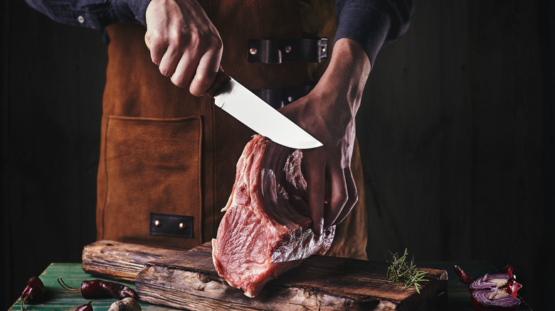 Person carving pork ribs on a wooden block