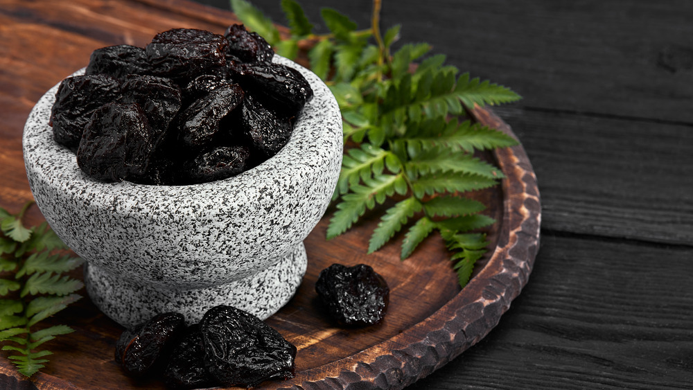 Gray bowl full of prunes on wooden slab