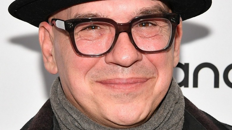 Michael Symon smiling wearing glasses and hat