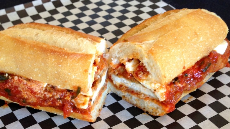 A chicken Parmesan sandwich cut in half on a piece of paper with a checkerboard pattern
