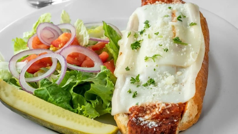 A chicken Parmesan sandwich with a side salad and pickle