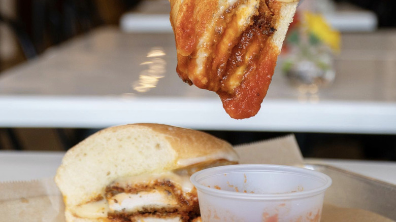 A chicken Parmesan sandwich being dipped in extra marinara