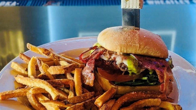 A knife going through the chicken Parmesan sandwich from Jams on a plate with fries