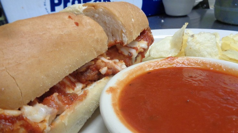 The Figaretti's chicken Parmesan sandwich on a plate with a bowl of marinara sauce and chips