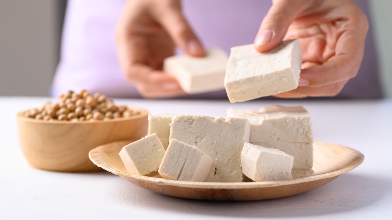 Person breaking up blocks of tofu on a plate