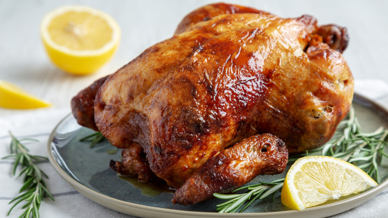 Roast chicken on a ceramic plate with lemon and herbs around it on a white tablecloth