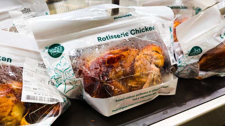 Rotisserie chickens in white Whole Foods Market bags on a warmer inside a supermarket