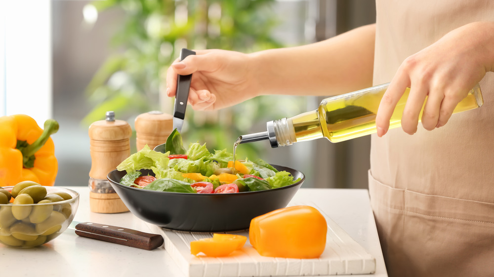 Person adding olive oil to salad