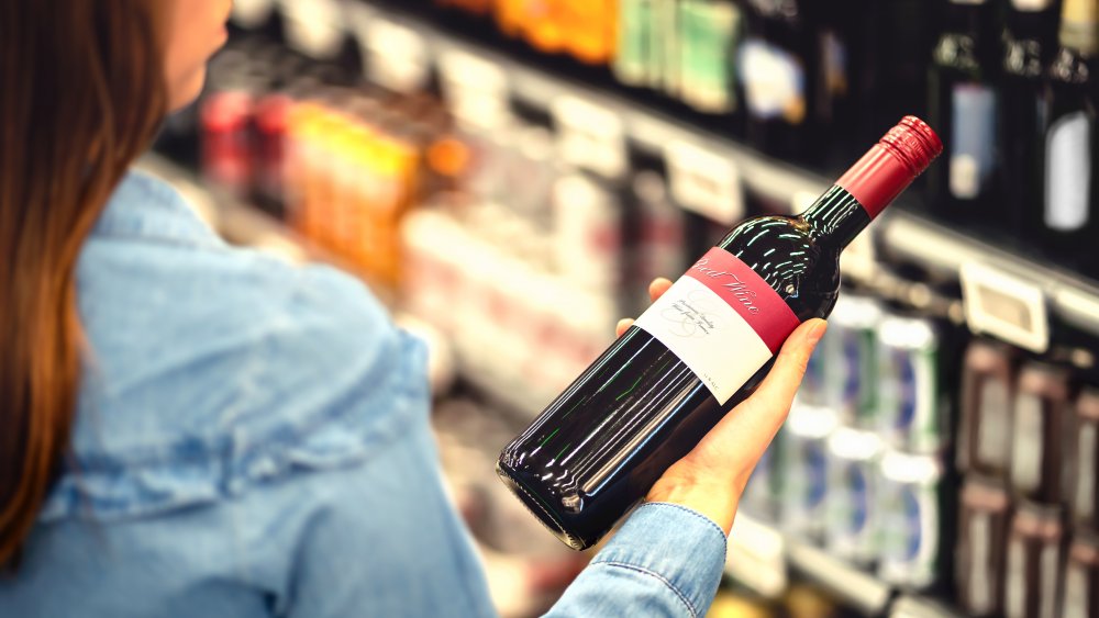 woman holding a bottle of red wine in a grocery store wine aisle