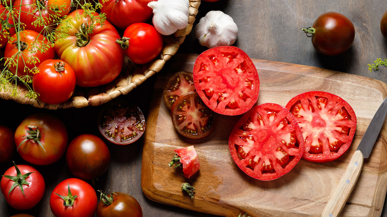 Tomatoes sliced and whole in basket on cutting board