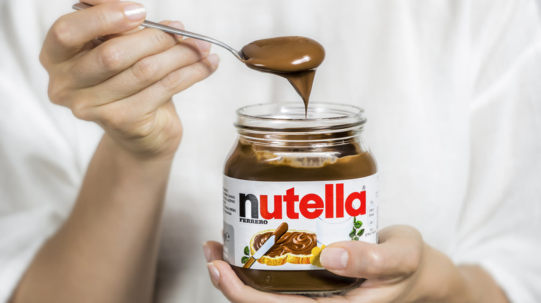 Person holding jar and spoonful of Nutella