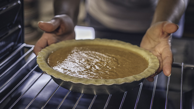 Person putting pumpkin pie in oven