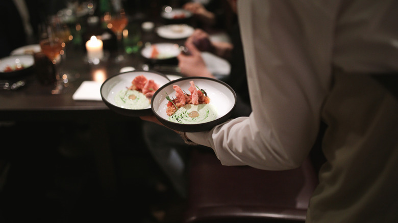 An unidentified waiter carrying two elegantly plated meals through a restaurant