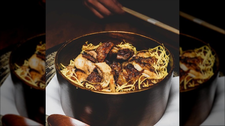 Habachi chicken over a bed of rice served in a black ceramic bowl
