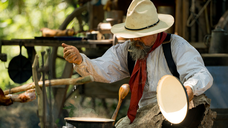A modern cowboy preparing food at a rustic outdoor campfire