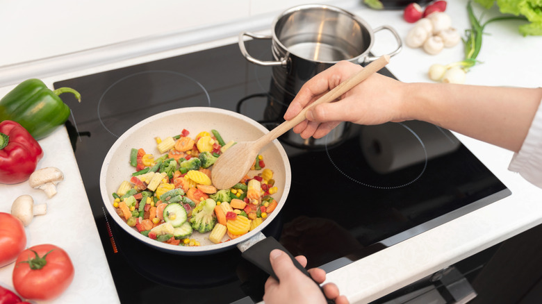 Person cooking vegetables in a pan on induction stove.
