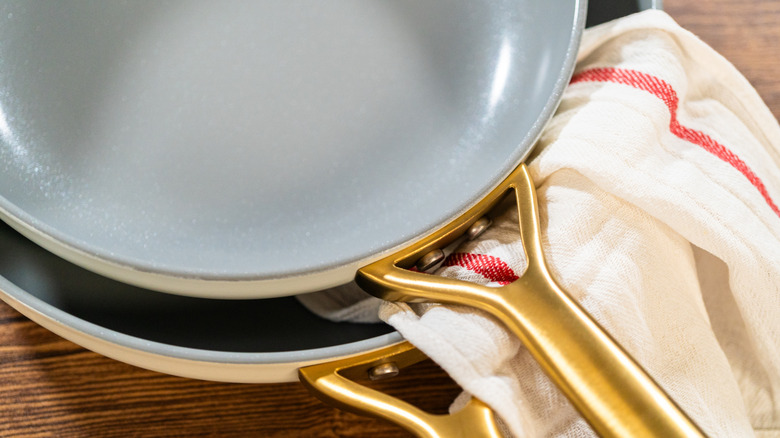 Two stacked ceramic frying pans with kitchen towel between them.