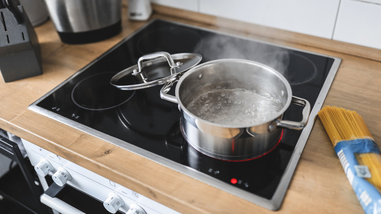 Pot of boiling water on induction stovetop next to opened package of uncooked pasta.