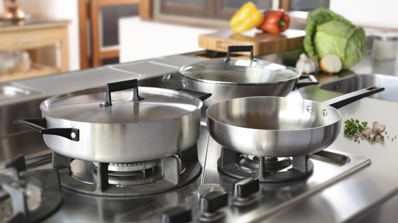 Aluminum pots and pans on gas burners in kitchen.
