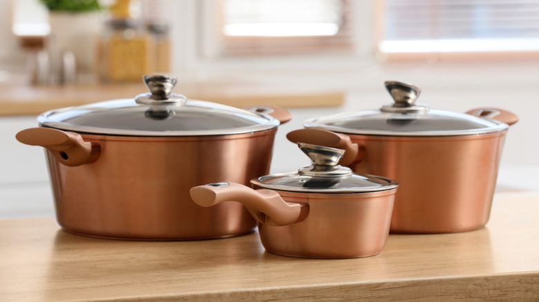 A copper cookware set with three differently sized pots with lids.