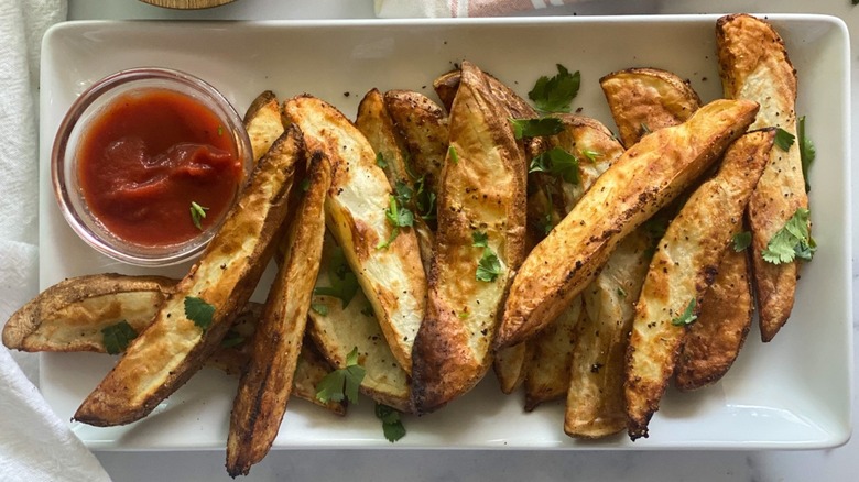 Steak fries on a plate with a small bowl of ketchup.