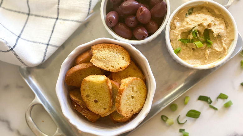 Homemade bagel chips served with olives and hummus on silver tray 