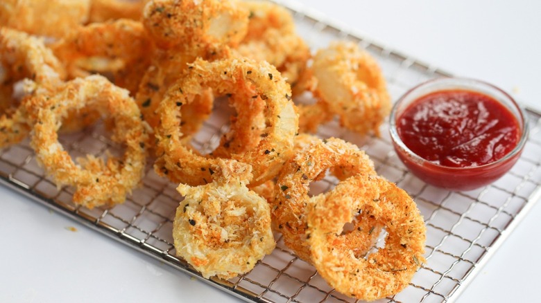 Baked onion rings on a serving tray with a small bowl of ketcup.