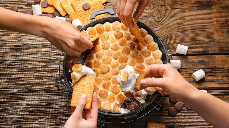 Hands dipping graham crackers in s'mores dip
