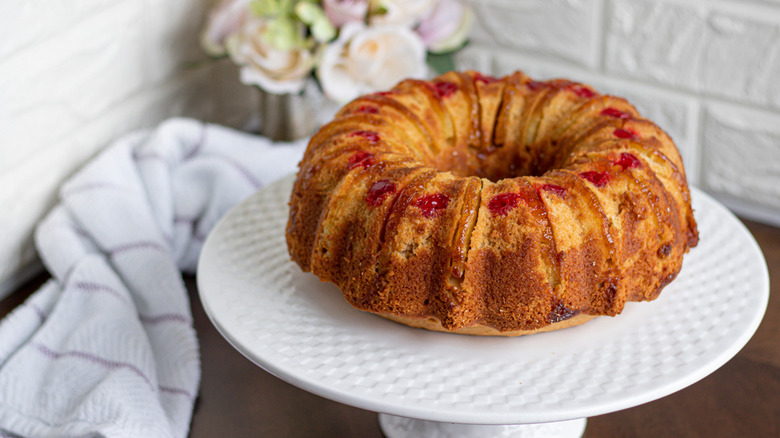 homemade pineapple upside down cake made from scratch on a white cake plate with a bouquet of flowers behind it