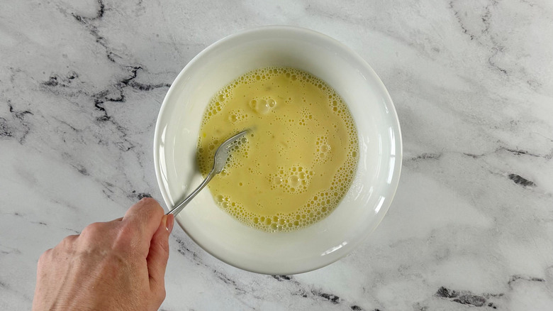 Hand using fork to whisk egg and milk mixture