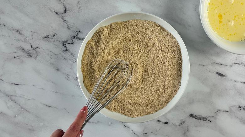 Hand whisking breadcrumb mixture in bowl