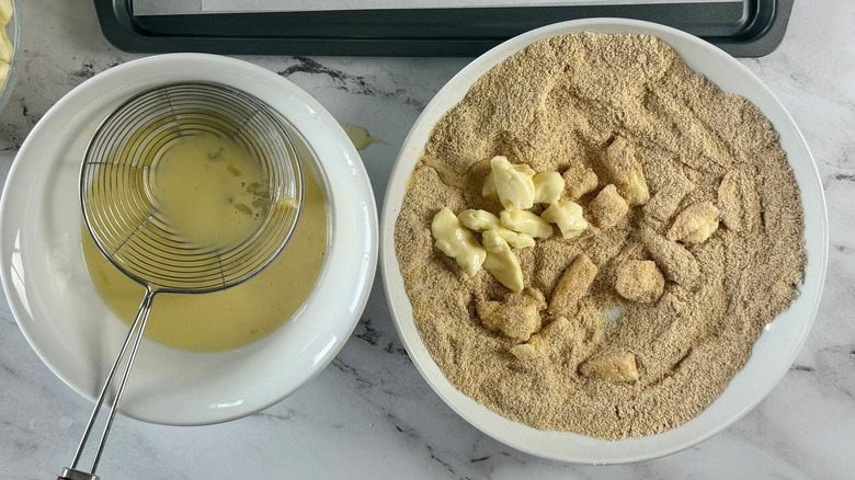 Egg mixture and strainer in bowl next to cheese curds in breadcrumbs