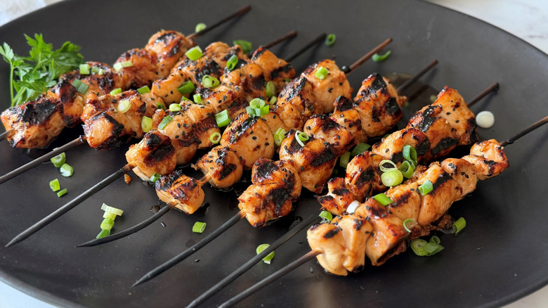 Honey garlic chicken skewers garnished with scallions on serving plate