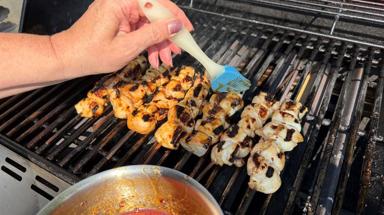 Brushing chicken skewers with glaze on grill