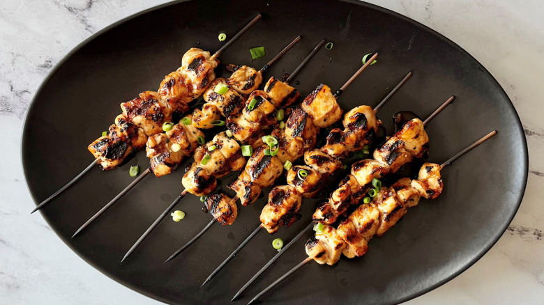 Honey garlic chicken skewers garnished with scallions on serving plate