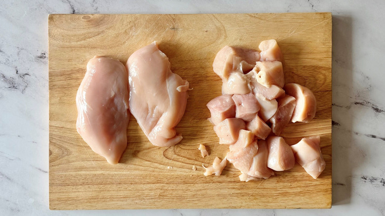 Whole and cubed chicken breasts on wooden board