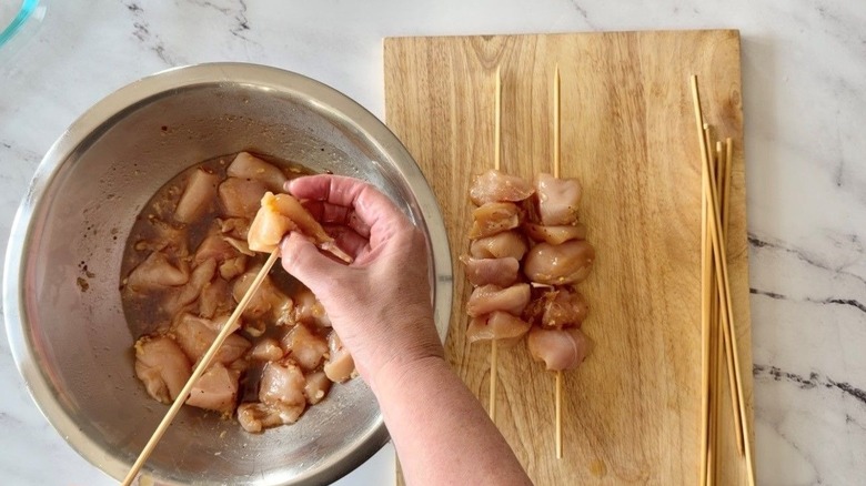 Hand threading chicken cube onto skewer